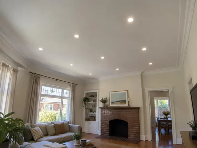 Living room ceiling with evenly spaced recessed downlights above a lounge and brick fireplace in Northbridge