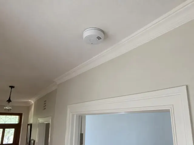 Ceiling smoke alarm in a hallway with cornice and door trim in Northbridge
