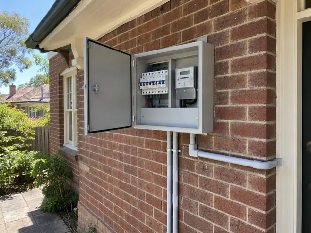 Open upgraded switchboard on a brick house exterior wall with conduit and breakers in Naremburn